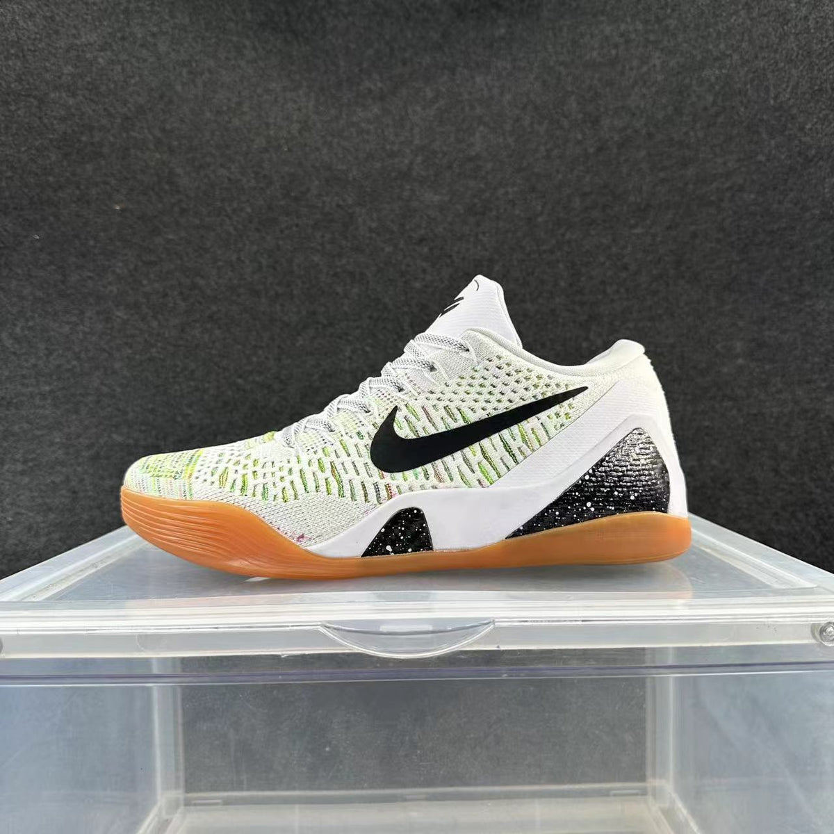White Nike basketball-style sneaker with black Swoosh branding, light green upper detailing, and a gum-colored outsole displayed on a clear stand.