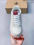Top view of the white lace-up sneaker showing the textured toe panel, white laces and burgundy tongue.