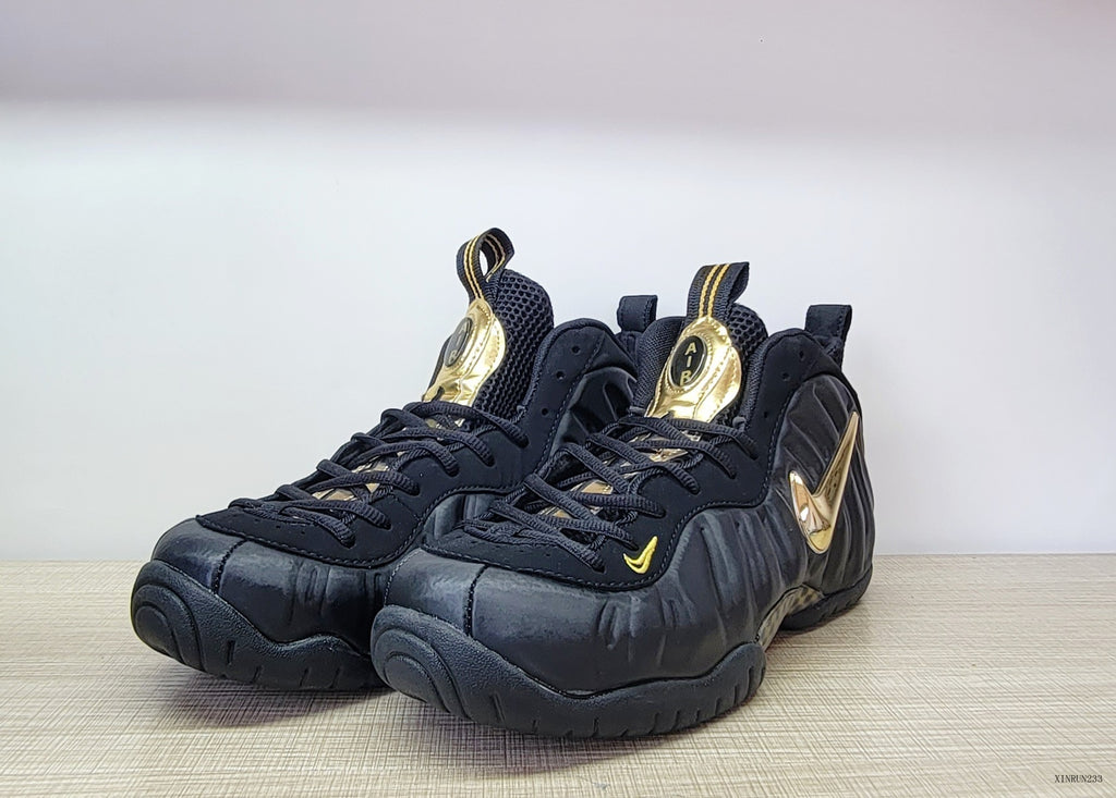 Three-quarter front view of black and metallic gold Nike Air Foamposite Pro sneakers