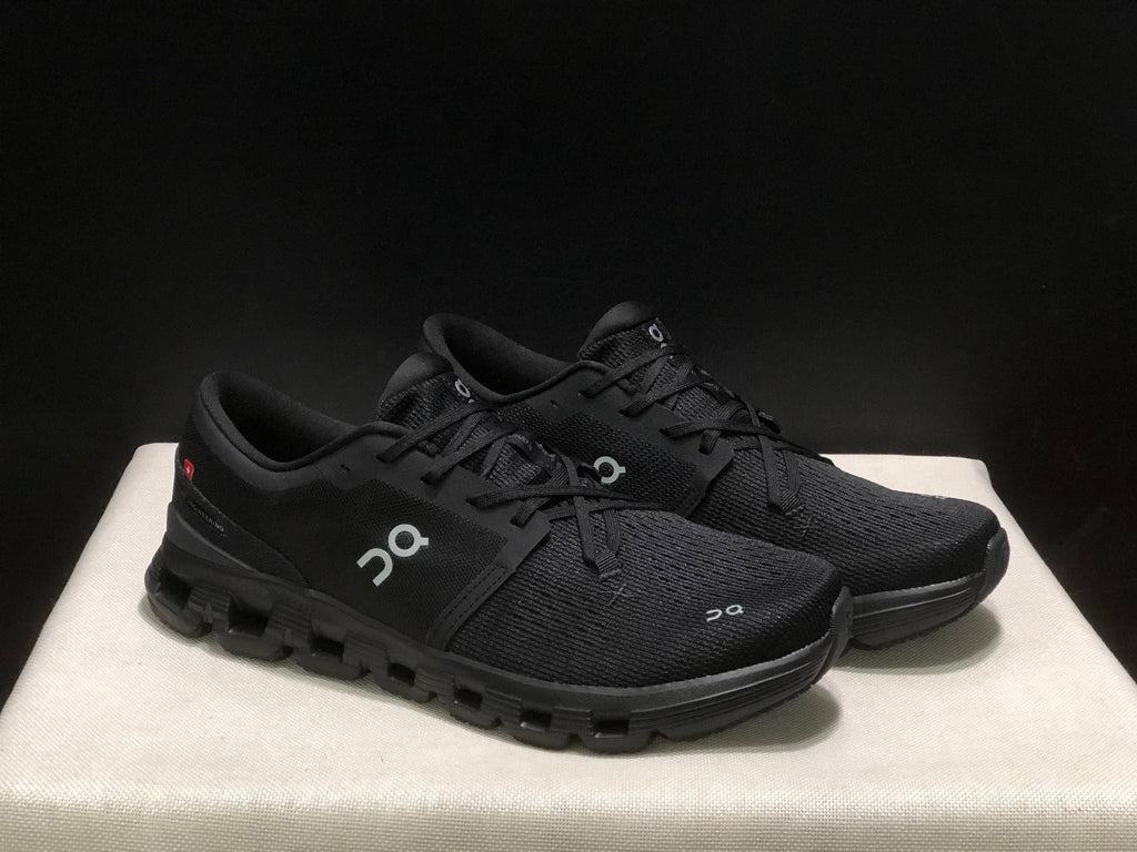 Three-quarter view of the black On Cloud X4 pair showing the uppers, laces and black outsoles.