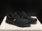 Three-quarter view of the black On Cloud X4 pair showing the uppers, laces and black outsoles.