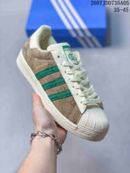 Angled side view showing the patterned beige upper, green stripes, shell toe, and off-white rubber sole.