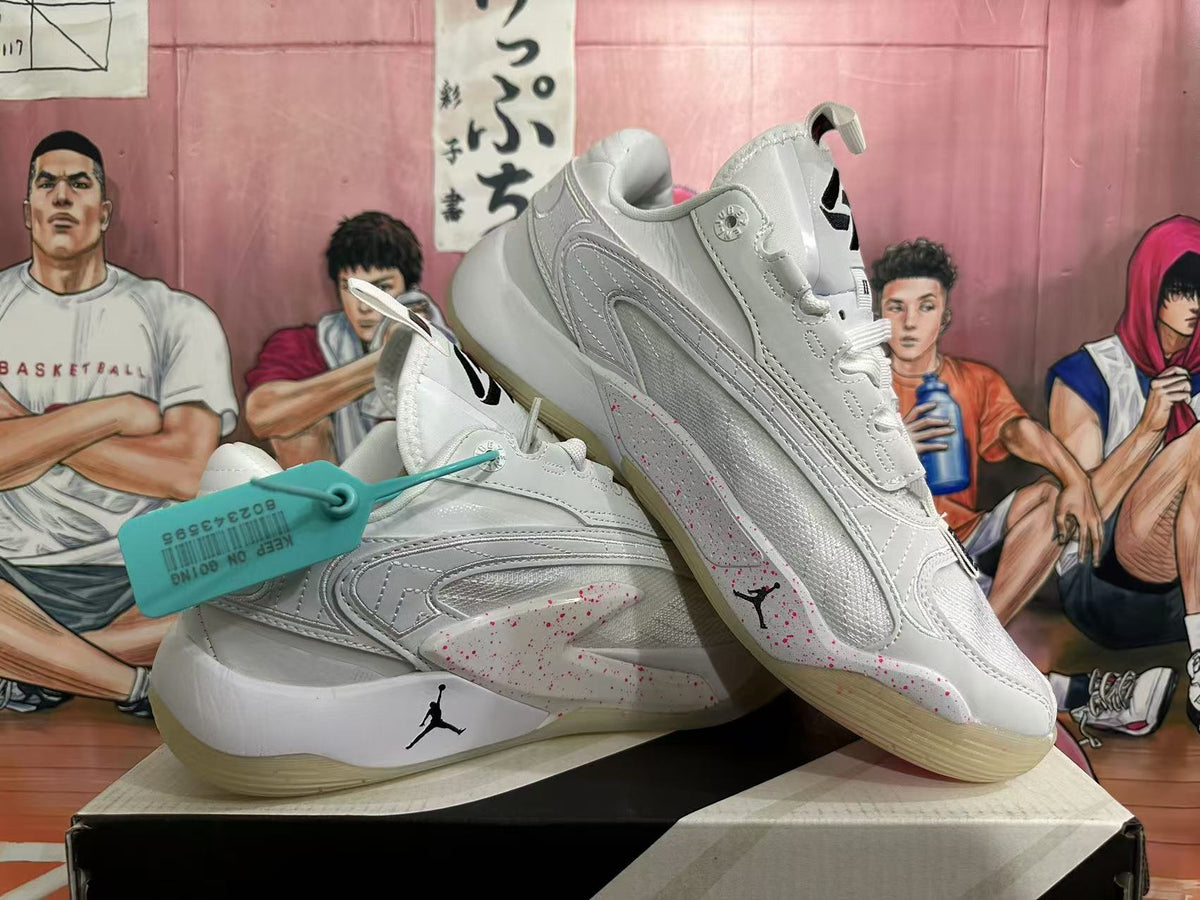 Angled view of a pair of white Jordan basketball sneakers with black Jumpman logos and red speckled side details.
