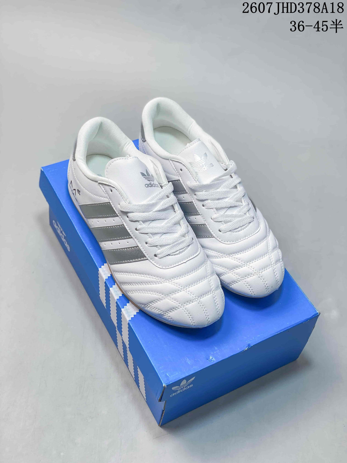 White adidas low-top sneakers with dark side stripes, laces and quilted toe detailing displayed on a blue shoebox.