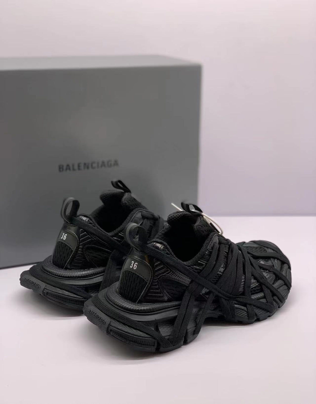 Angled rear-side view of the black sneakers showing heel details and layered laces.