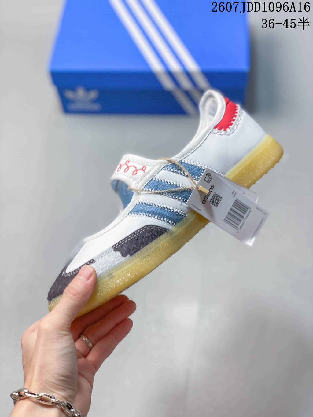 Side view of the sneaker showing the blue stripes, red heel accent, hook-and-loop strap, and attached product tag.