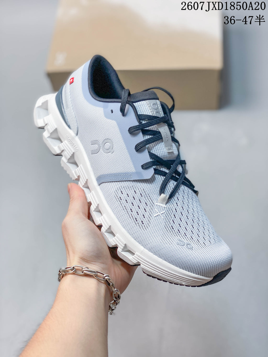 Angled side view of the On Cloud X 4 sneaker showing its light gray upper, navy details, and white segmented outsole.
