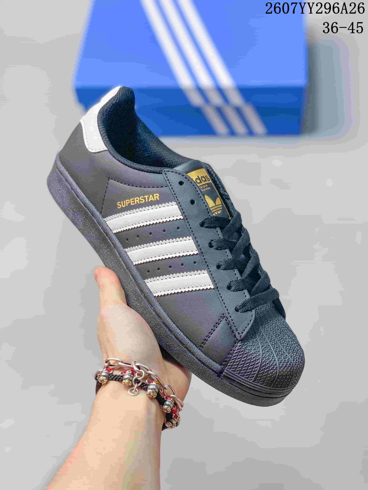 Angled side view of the black sneaker showing SUPERSTAR side branding, white stripes, textured toe cap, and white heel tab.