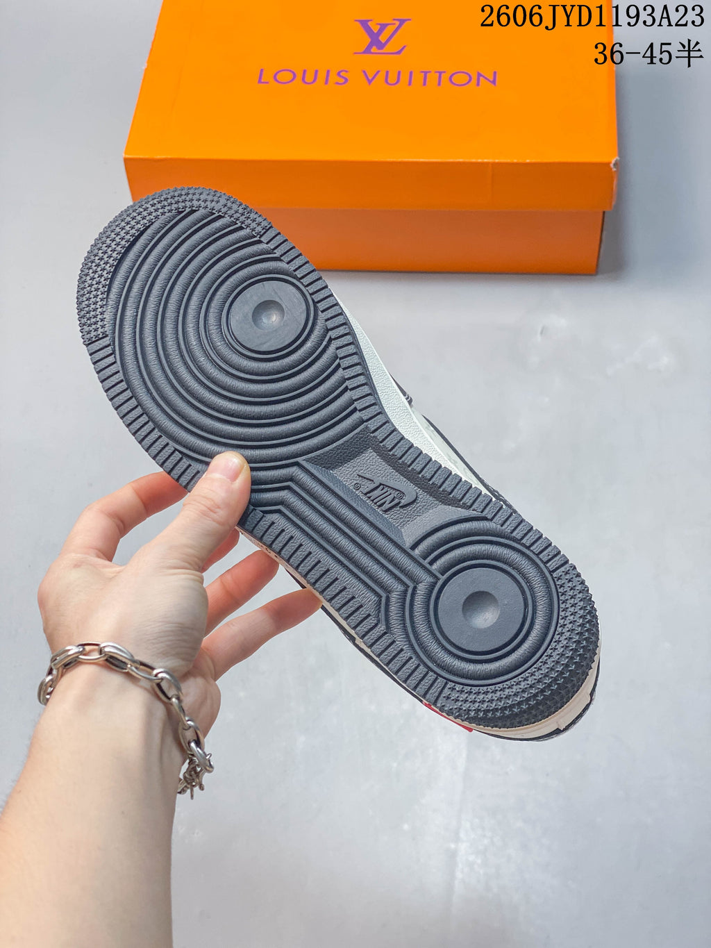Underside of a cream and charcoal low-top sneaker showing the dark patterned outsole