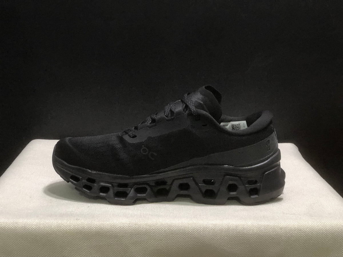 Side profile of a single black sneaker showing its padded collar, side branding and outsole structure.