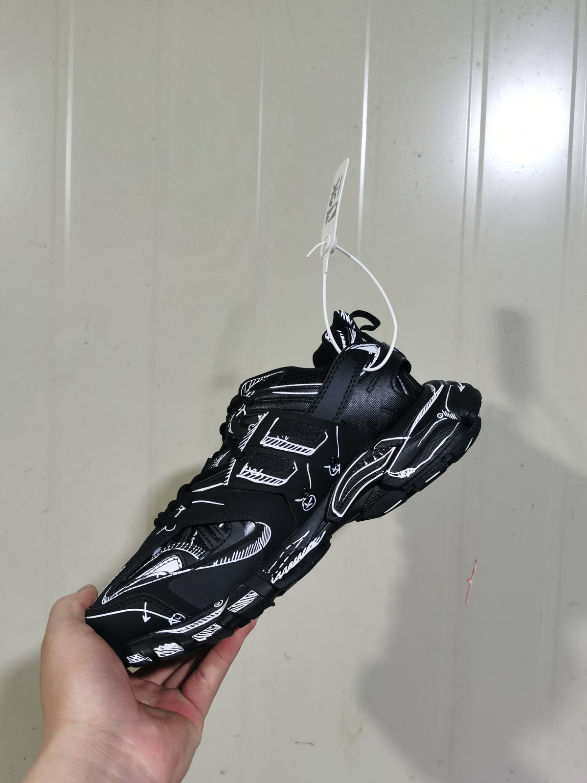 Top and rear view of the black and white track sneaker showing the layered construction, heel details, outsole, and attached product tag.