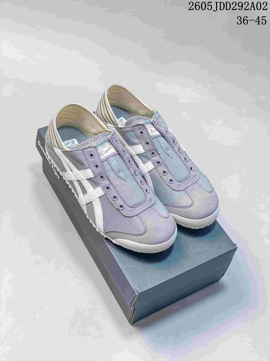Pair of gray Onitsuka Tiger slip-on sneakers with white side stripes, shown on a branded shoebox.