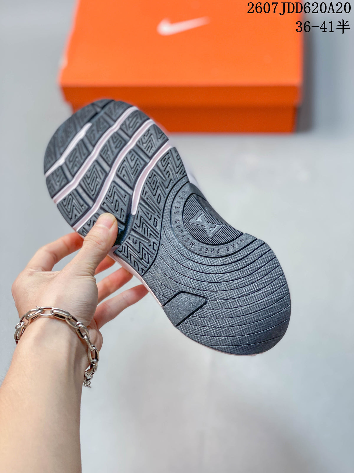 Close view of the dark patterned outsole on a pink and white training shoe, with the orange shoebox in the background.