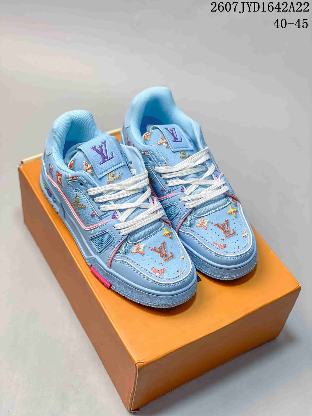 Pair of light blue Louis Vuitton Trainer low-top sneakers with white laces and multicolor patterned detailing on an orange shoe box.