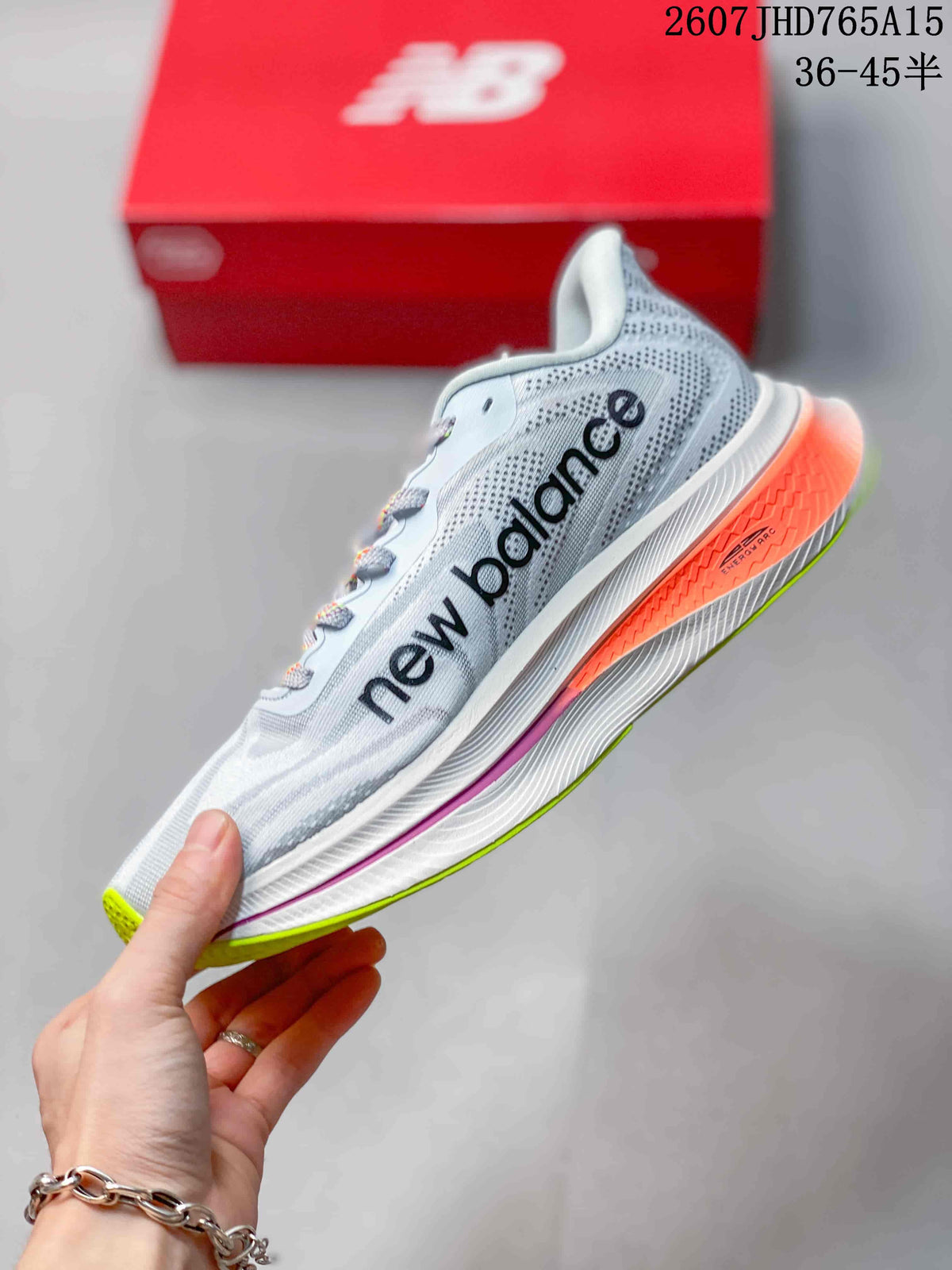 Side profile of the New Balance running shoe showing the large logo, light upper, orange heel detail, and layered midsole.