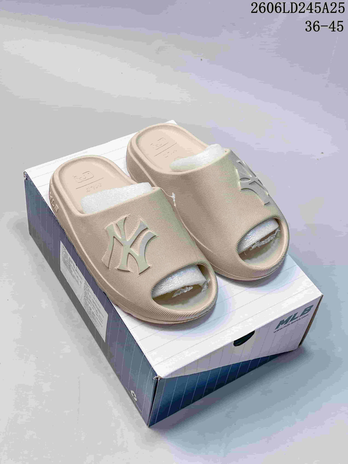 Beige open-toe slide sandals with raised NY lettering, displayed on a box.