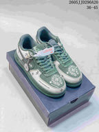 Pair of green and white low-top sneakers displayed on a shoebox, with layered panels, decorative graphics, and attached accessories.