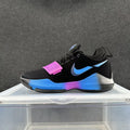 Side view of a black Nike sneaker with a blue Swoosh, pink forefoot strap, and blue and pink sole accents.
