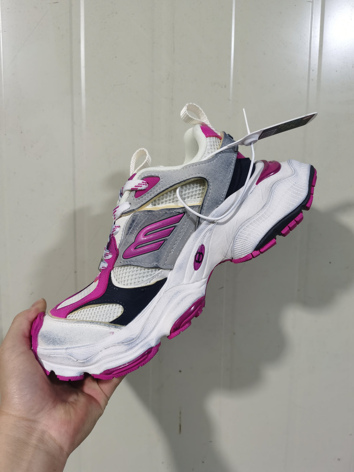 Close-up view of grey, white, black and pink Balenciaga sneakers showing layered panels, mesh sections and a chunky outsole.