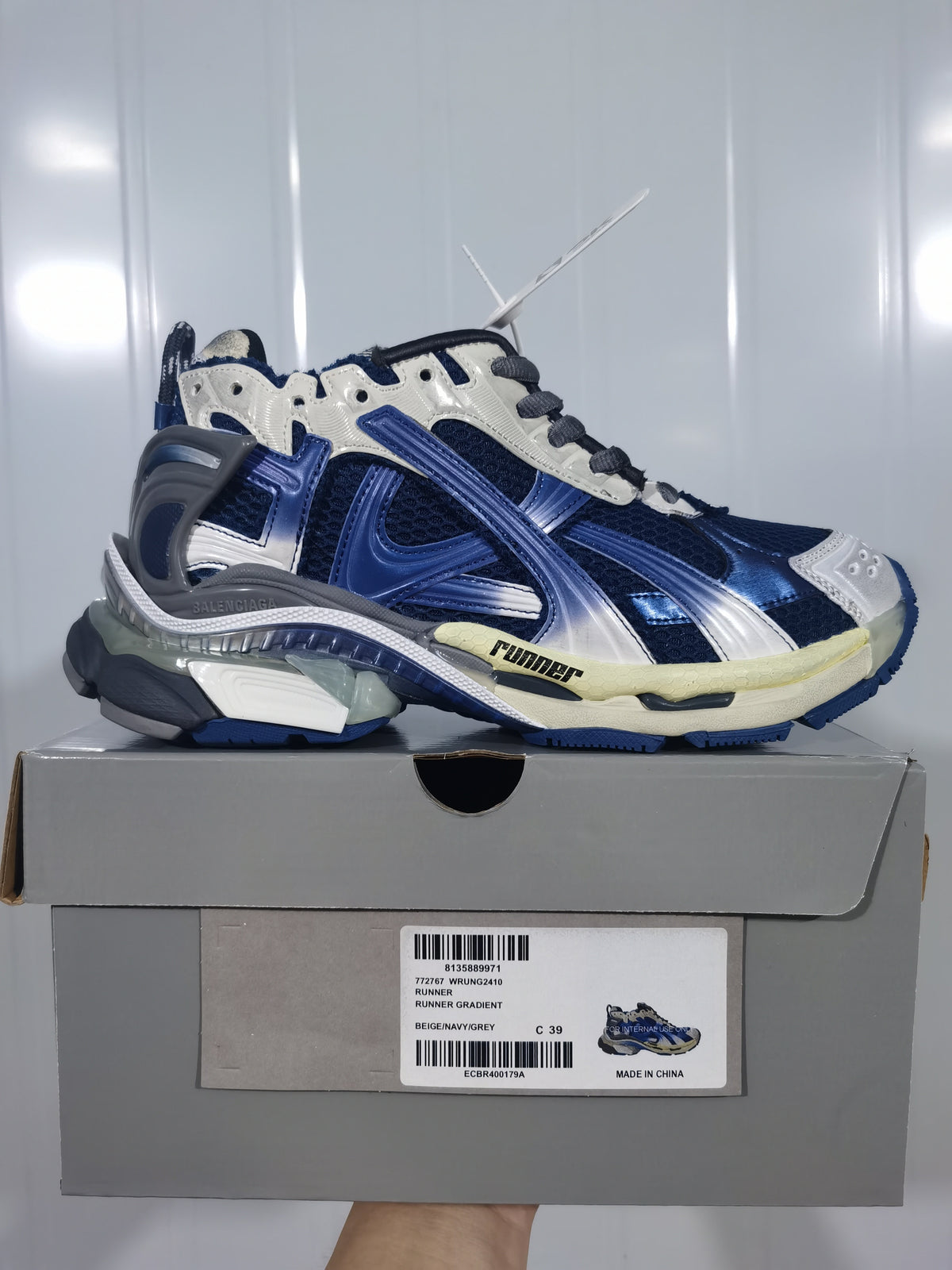 Balenciaga Runner sneaker in beige, navy and grey displayed on its shoe box; the box label shows size C 39.
