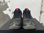 Front view showing the textured dark camouflage upper, black laces, and red tongue emblems.
