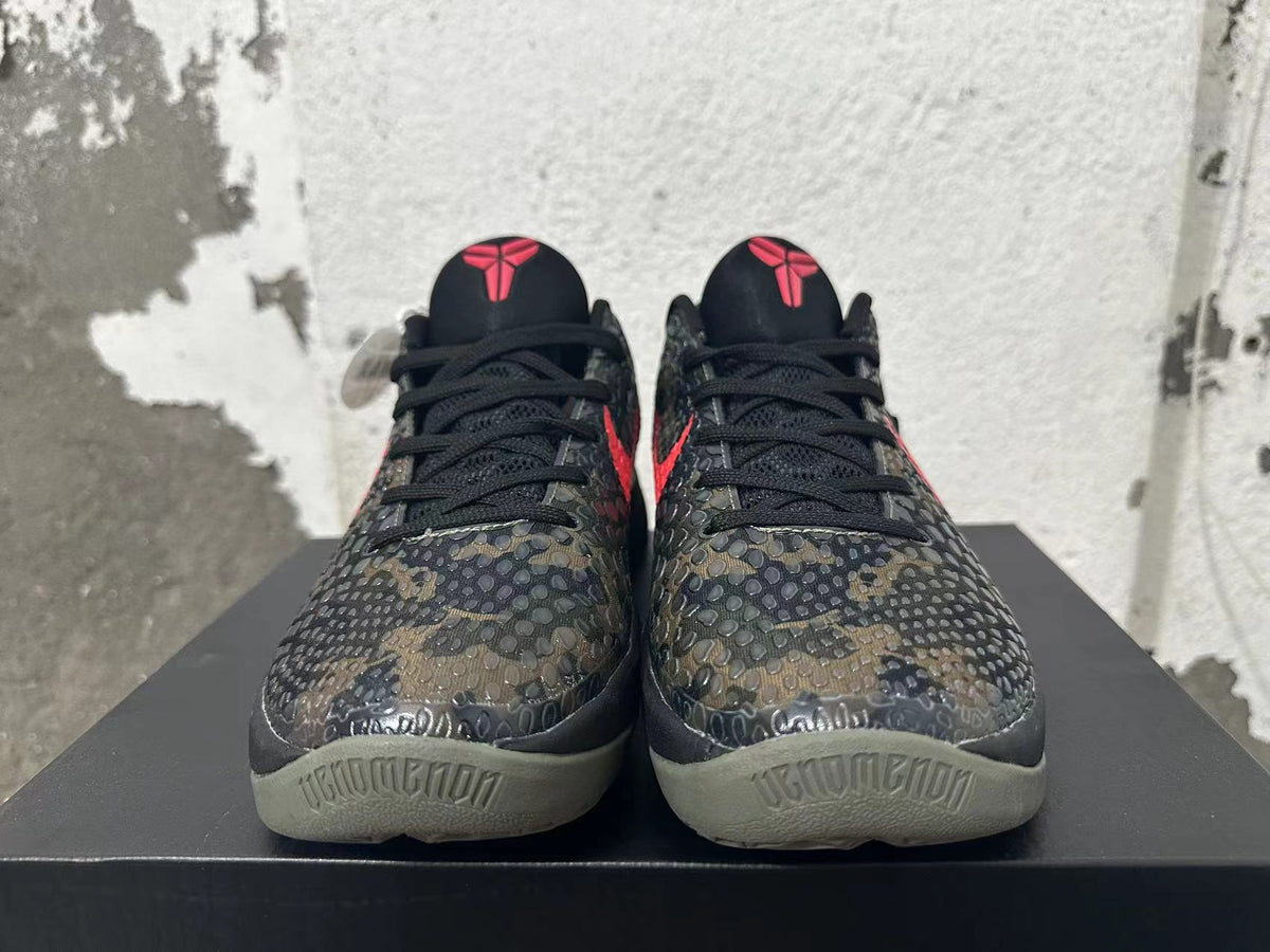 Front view showing the textured dark camouflage upper, black laces, and red tongue emblems.