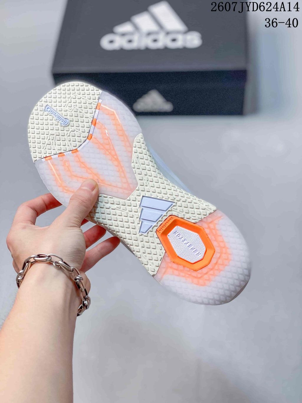 Bottom view of the white training shoe showing the textured outsole, orange accent sections, and adidas branding.