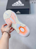 Bottom view of the white training shoe showing the textured outsole, orange accent sections, and adidas branding.