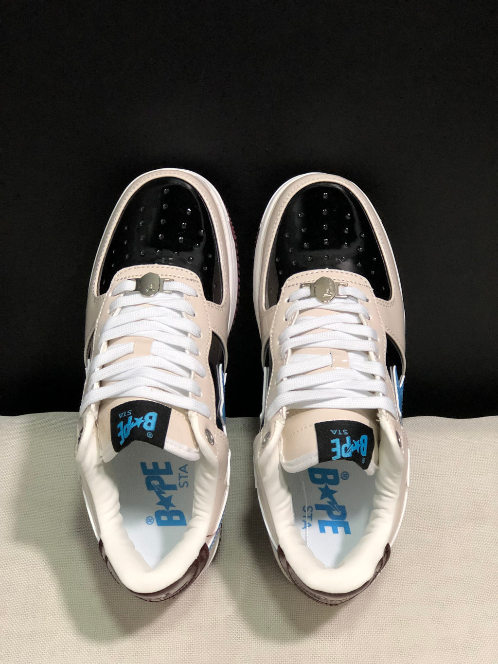 Top view showing the black perforated toe panels, cream overlays, white laces, and blue Bape Sta insole branding.