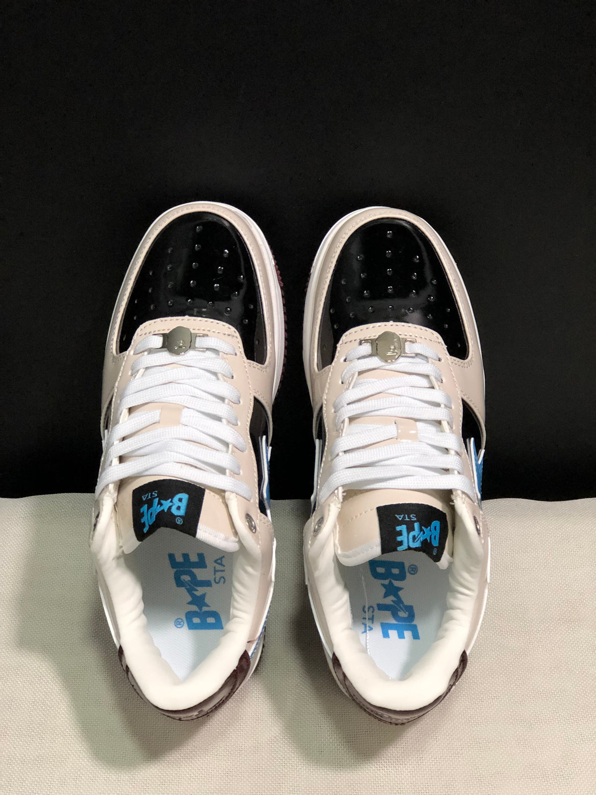 Top view showing the black perforated toe panels, cream overlays, white laces, and blue Bape Sta insole branding.