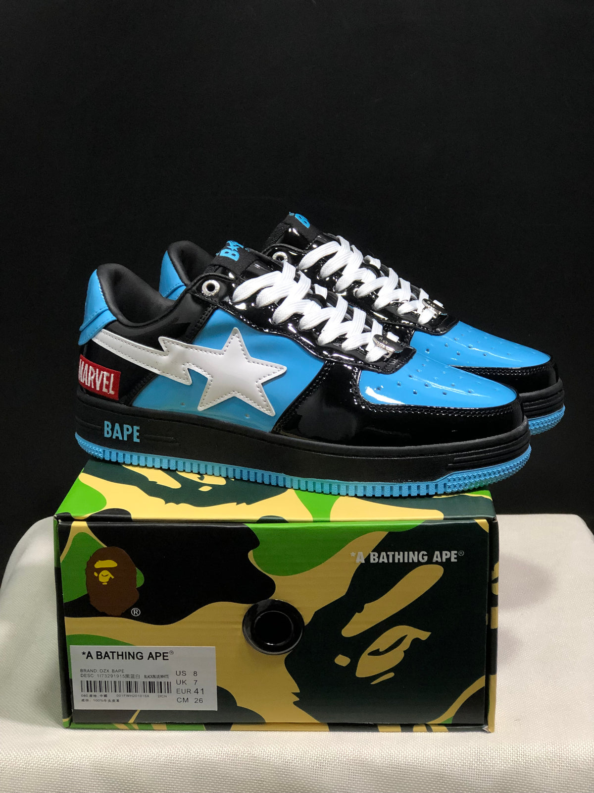 Black, blue, and white BAPE STA sneakers displayed on a camouflage BAPE shoe box; the box label shows a sample size of US 8, UK 7, EU 41, and CM 26.
