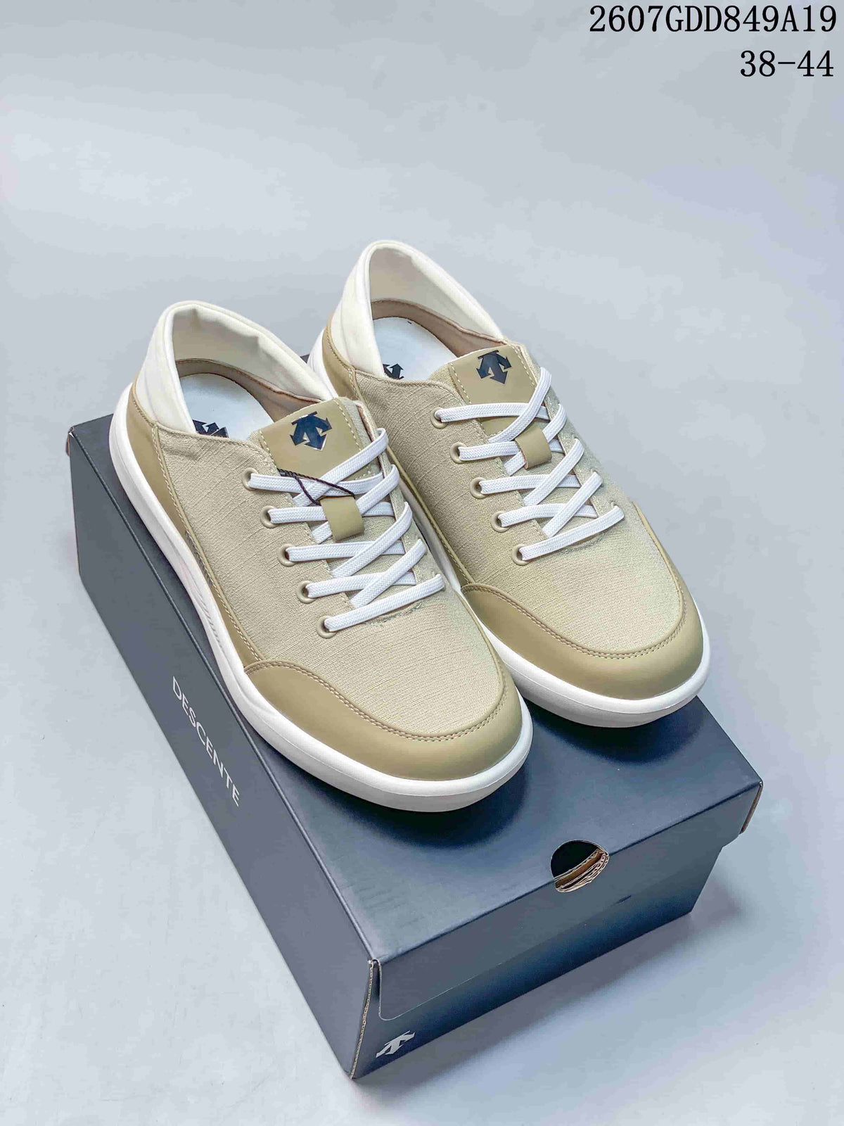 Pair of beige Descente low-top sneakers displayed on a shoebox, with style code 2607GDD849A19 and size range 38–44 visible.