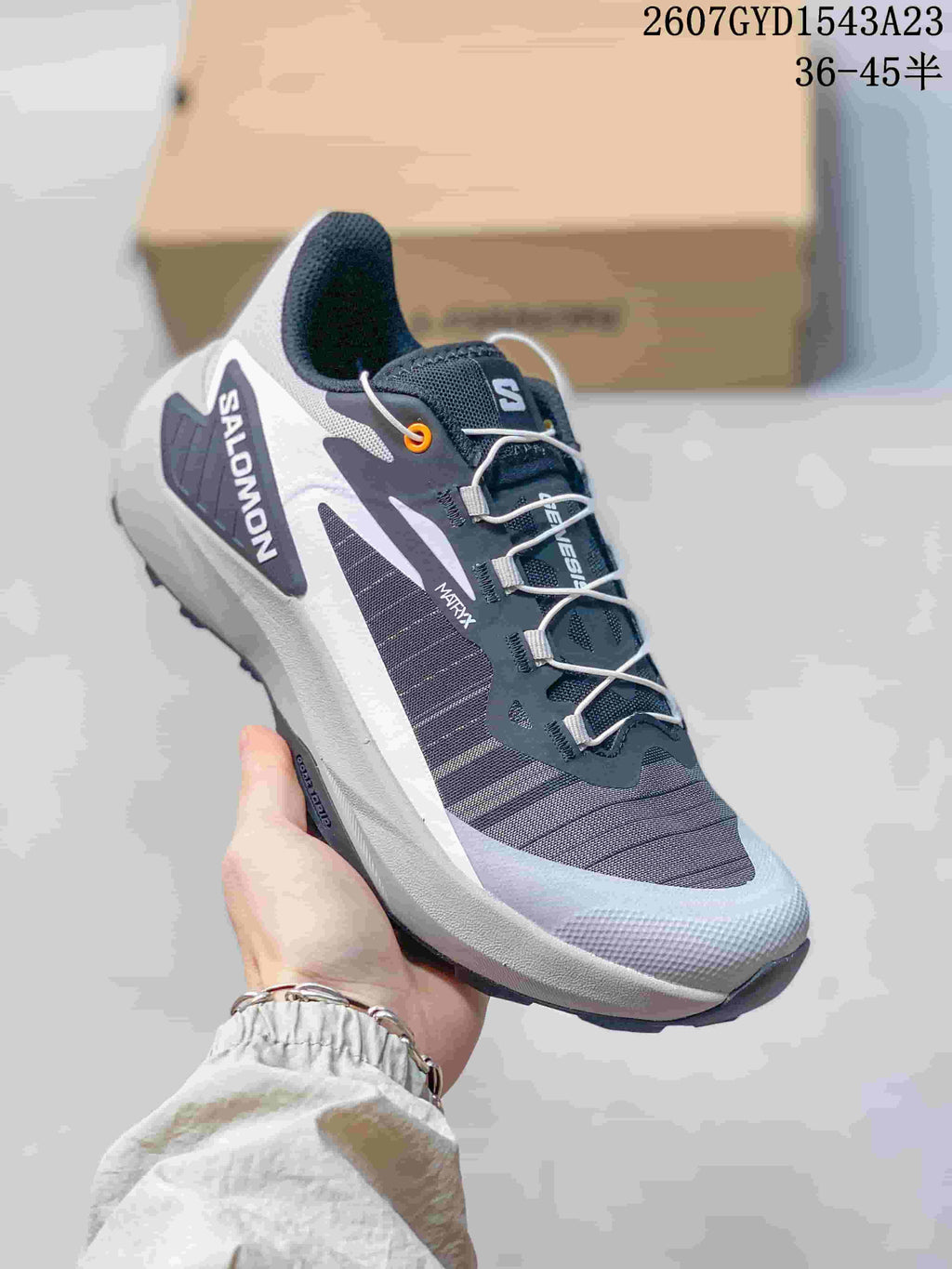 White and dark gray Salomon Genesis shoe with orange eyelet detail and white laces.