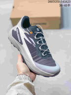White and dark gray Salomon Genesis shoe with orange eyelet detail and white laces.