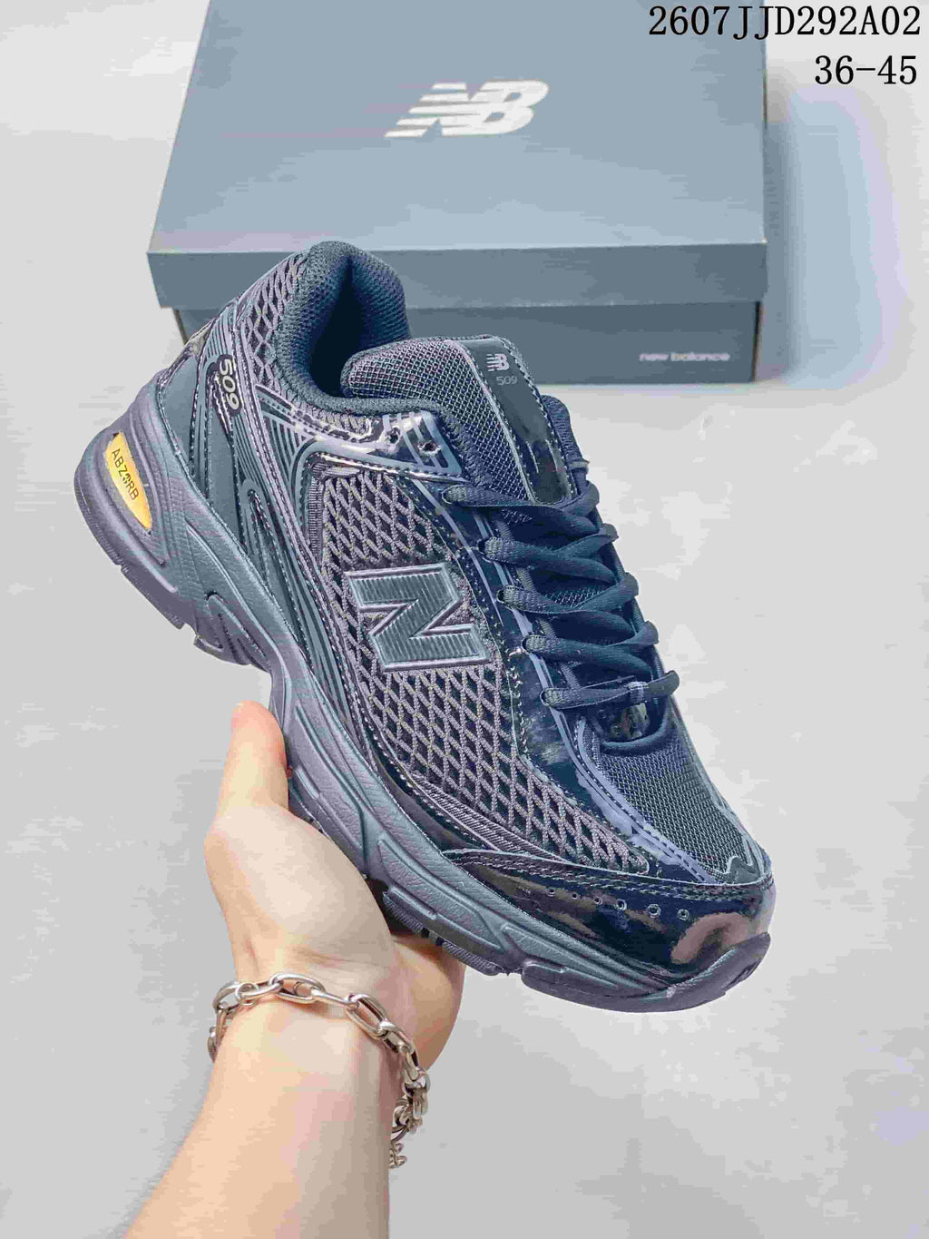 Front three-quarter view of the dark gray New Balance 509 sneaker showing the large N logo, mesh side panel, padded collar, and yellow heel detail.