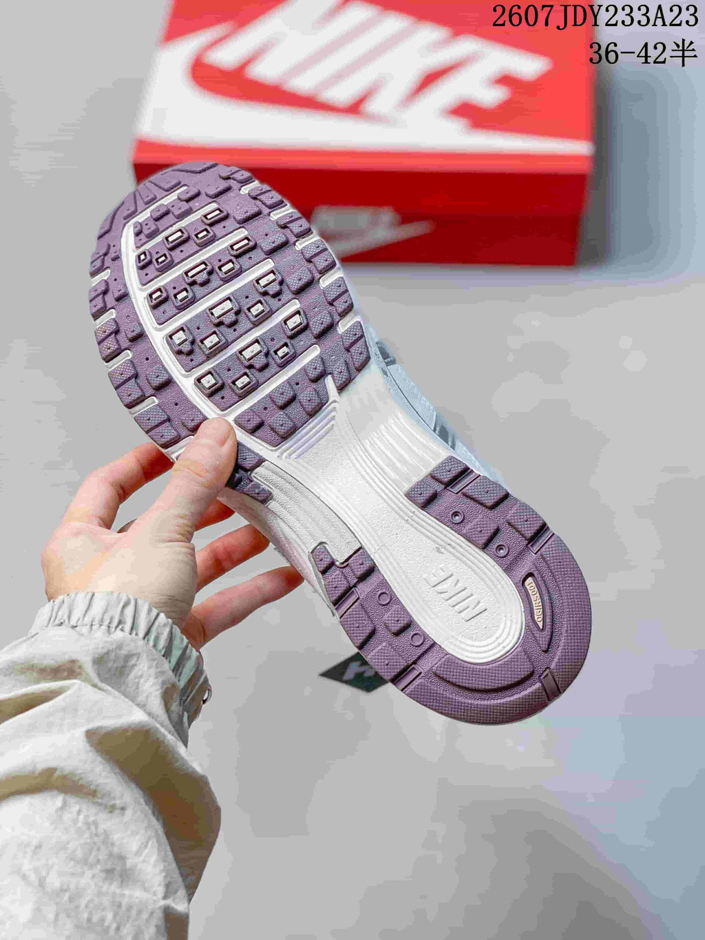 Close-up of the textured outsole on a silver and white sneaker, with the red Nike shoebox in the background; size range 36–42.5 is visible.