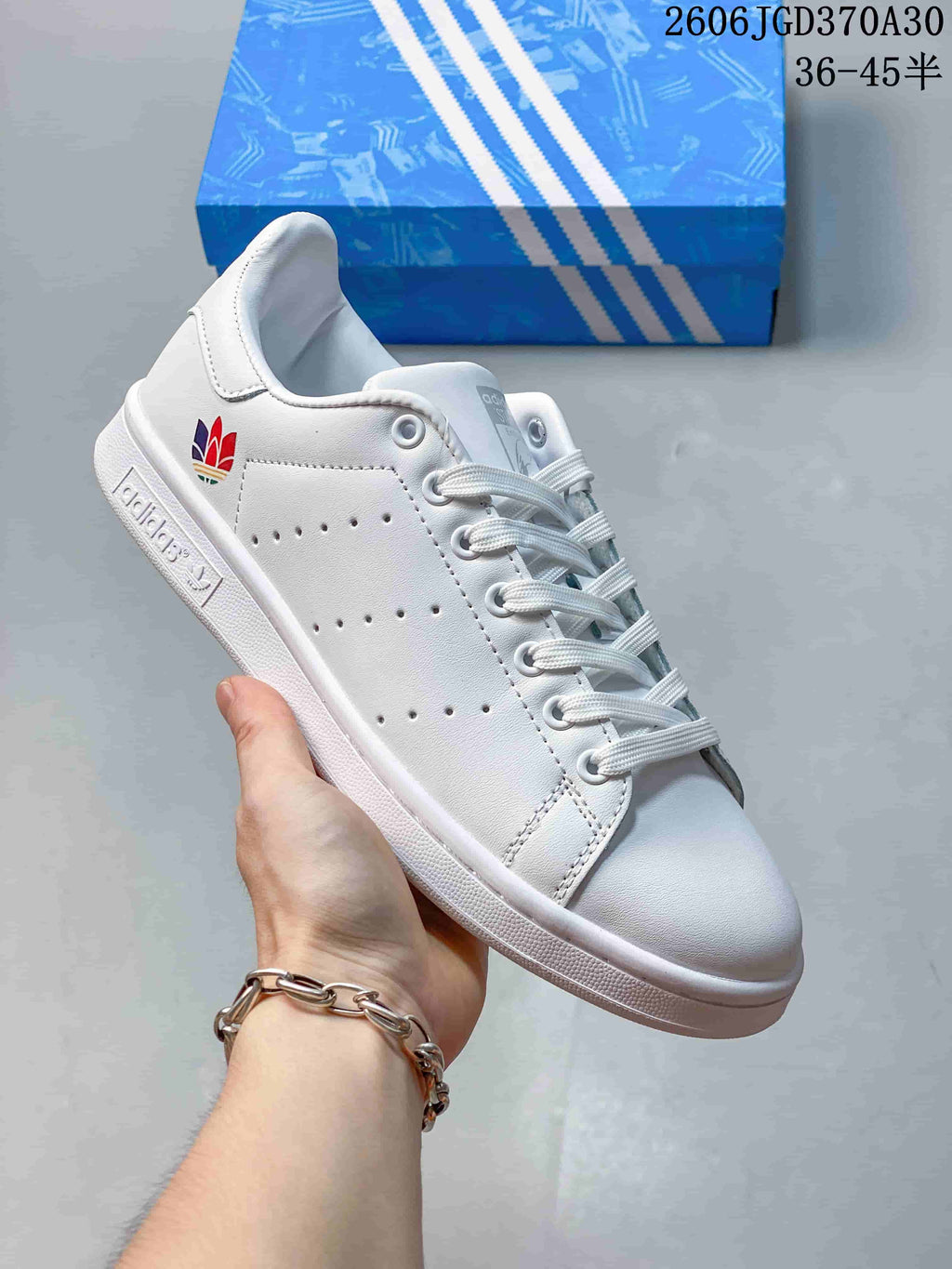 White Stan Smith-style sneaker with a multicolor heel emblem and a blue heel tab.