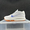 Side view of a white knit Nike sneaker with a blue Swoosh and orange outsole accents.