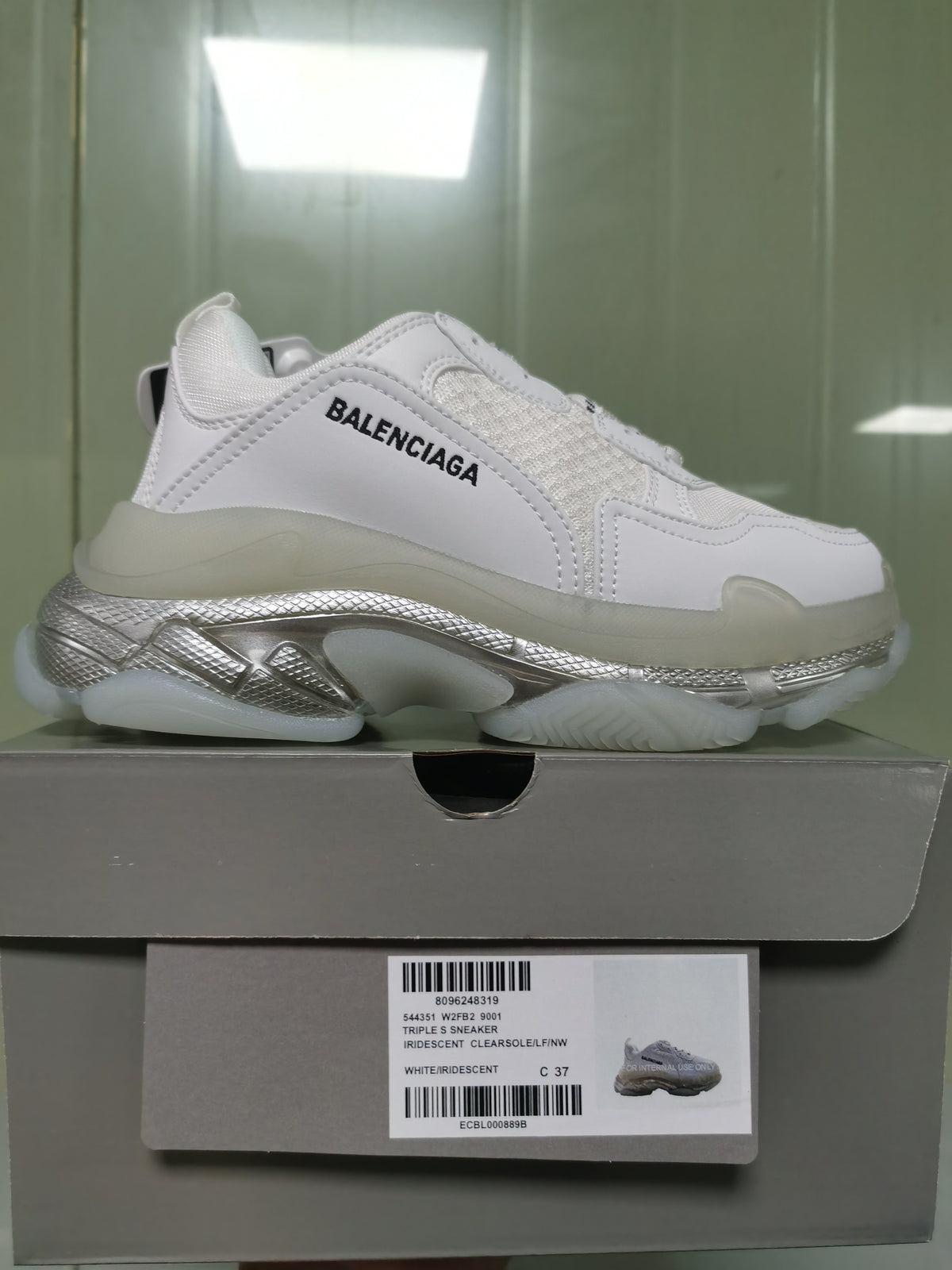 White Balenciaga Triple S sneaker shown on its box, with black branding, iridescent silver-toned sole details, and a box label showing size C 37 and style 9001.