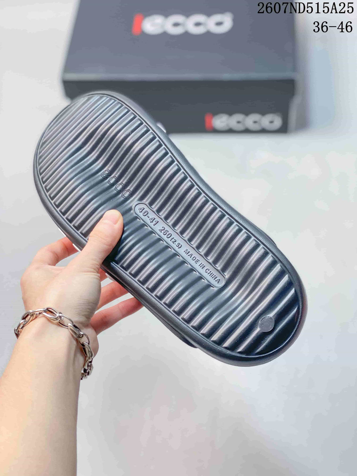 Bottom view of a dark slide sandal showing the ribbed outsole, molded footbed, ECCO marking, and a Made in China marking.
