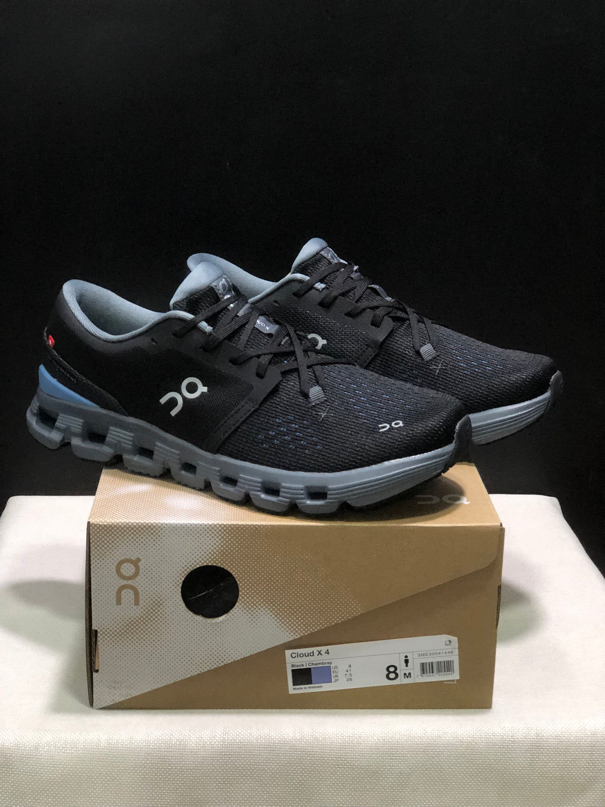 Pair of black and blue On Cloud X4 running shoes displayed on the product box.