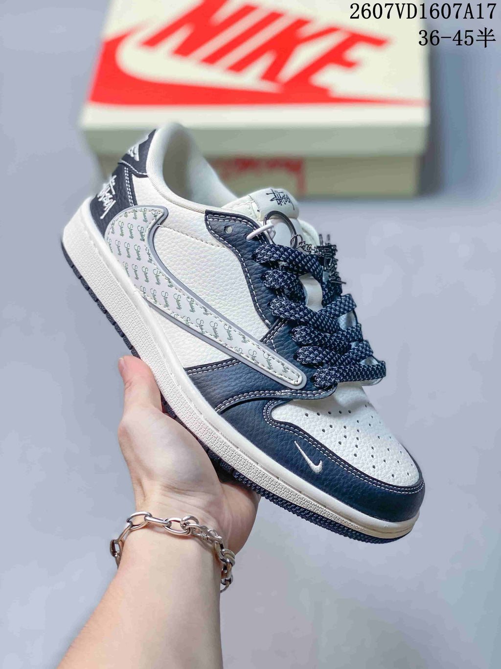 White and dark navy low-top sneaker with patterned side overlay, navy toe detail, dark laces and metal lace accessories.