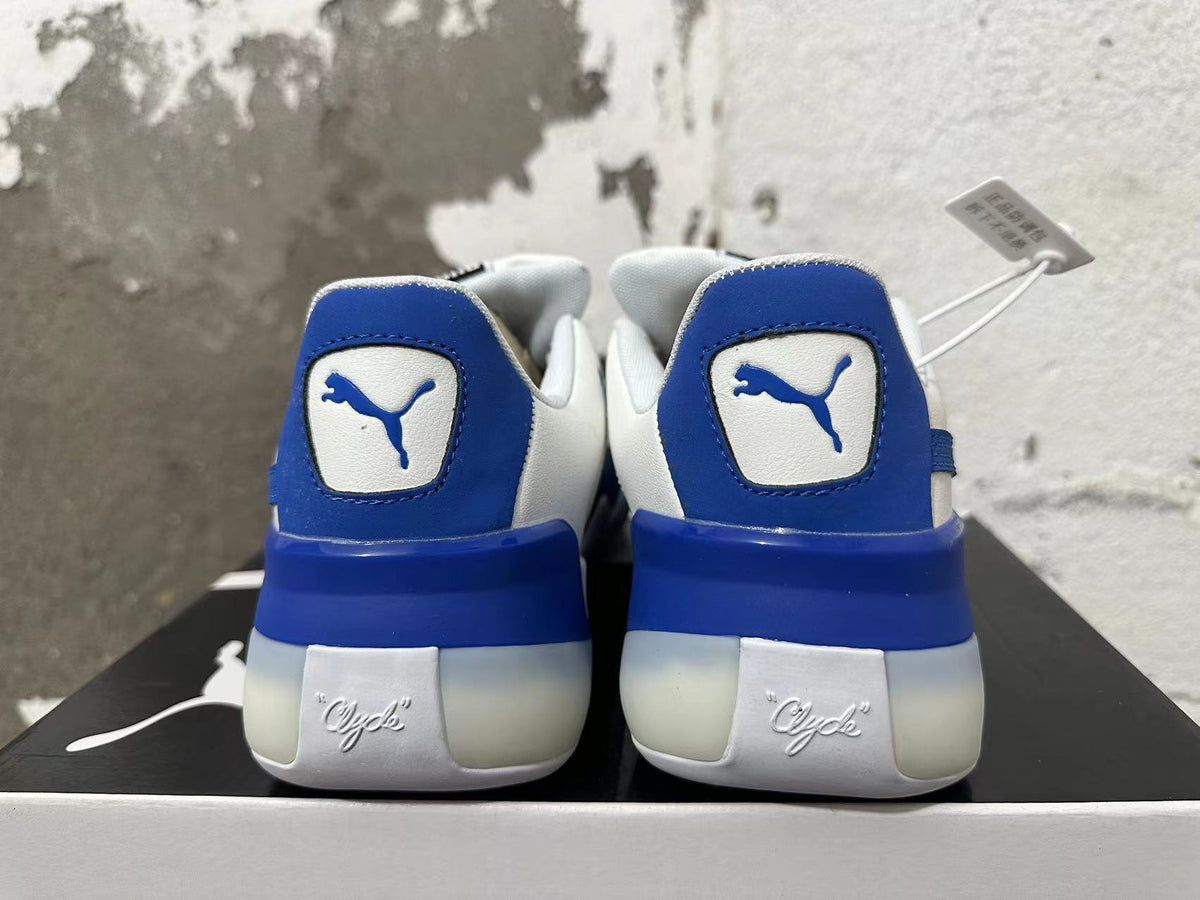 Rear view of white and blue Puma Clyde sneakers showing blue heel panels and Clyde lettering.