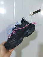 Black Balenciaga Track Trail sneaker shown from an angled side view with layered panels, chunky sole, and pink and blue rope-style laces.