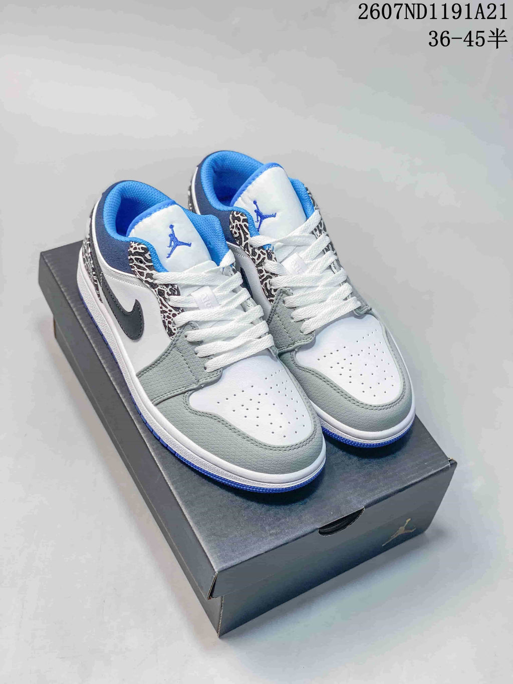 Pair of low-top Jordan sneakers on a shoebox, showing white, grey, blue and black panels with elephant-print detailing.