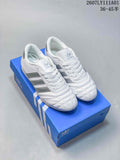 Pair of white Adidas Taekwondo low-top sneakers with silver stripes and quilted toes on a blue shoe box.
