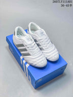 Pair of white Adidas Taekwondo low-top sneakers with silver stripes and quilted toes on a blue shoe box.