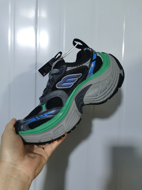 Black, green, blue, and gray chunky sneaker shown from the side in hand.