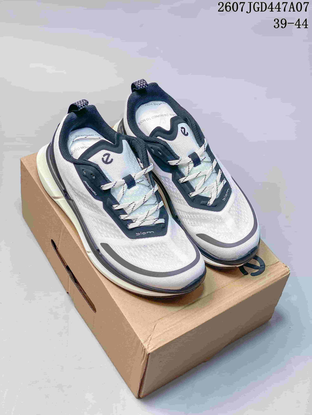 Pair of white, navy, and gray ECCO sneakers displayed on a cardboard shoebox; the image shows style code 2607TGD447A07 and size range 39-44.