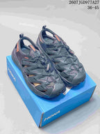 Pair of black and charcoal HOKA Hopara OG sandals displayed on a blue shoebox; image text shows style code 2607JGD977A27 and EU size range 36–45.